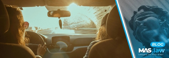 Two people driving with the sun shining on the windshield | MAS Law