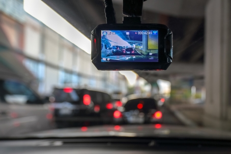 A dashcam mounted on a car windshield recording traffic under an overpass during heavy congestion.
